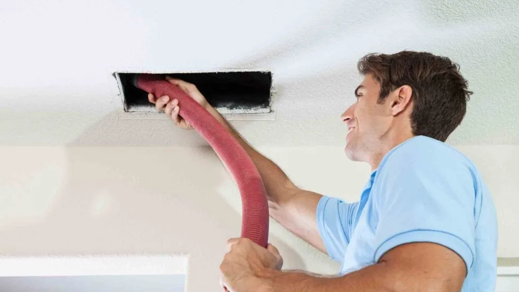 Technician feeding a red vacuum hose into a ceiling air duct