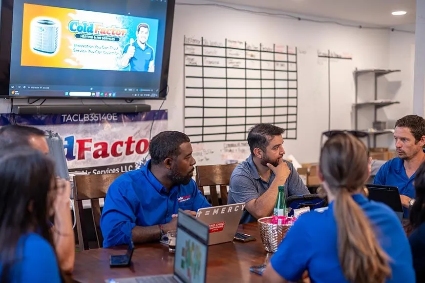 Cold Factor Heating & Air Services team gathered around a table for a meeting with the company logo visible on a TV screen — Cold Factor HVAC team in Flower Mound, TX