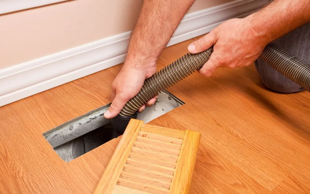 Hands feeding a vacuum hose into a floor air vent