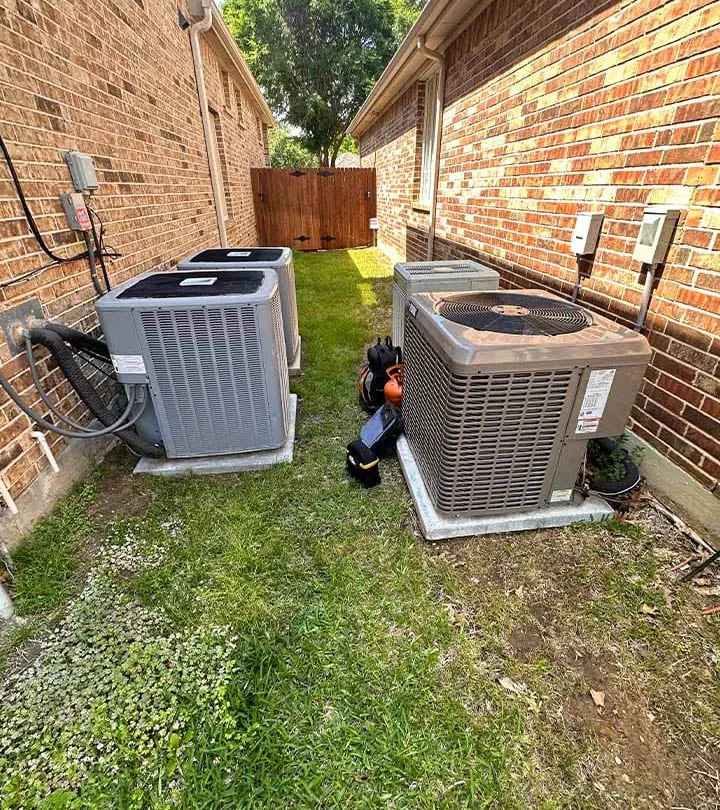 Two outdoor AC condenser units installed along the side of a brick home in Flower Mound TX -- Cold Factor AC repair and installation