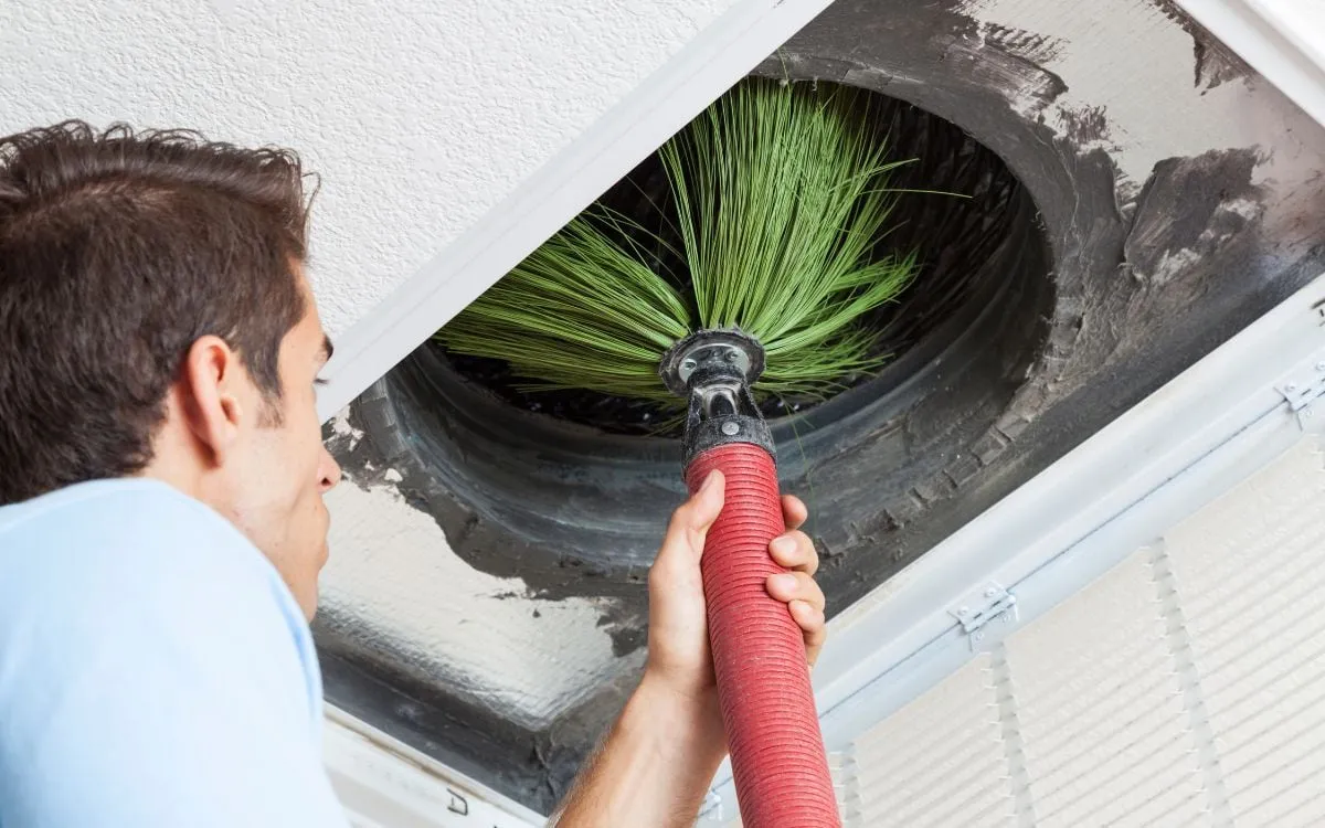 Technician cleaning a ceiling air duct with a rotary brush