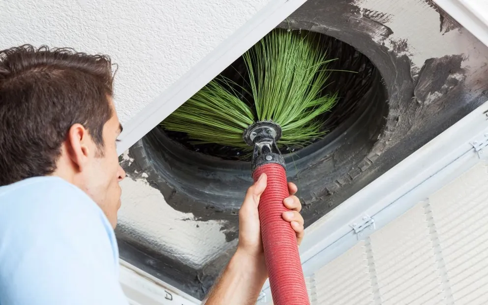 Technician cleaning a ceiling air duct with a rotary brush