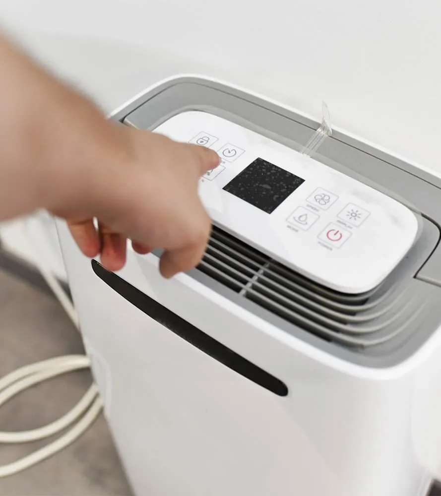 Homeowner adjusting controls on a portable dehumidifier -- Cold Factor indoor air quality services