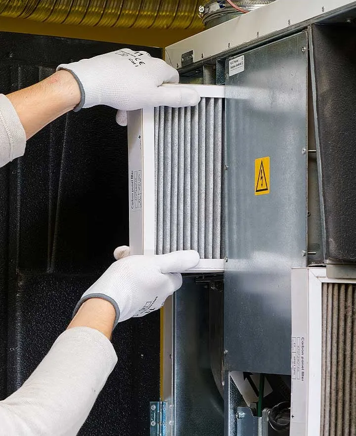 Technician installing a fresh carbon panel air filter into an HVAC unit