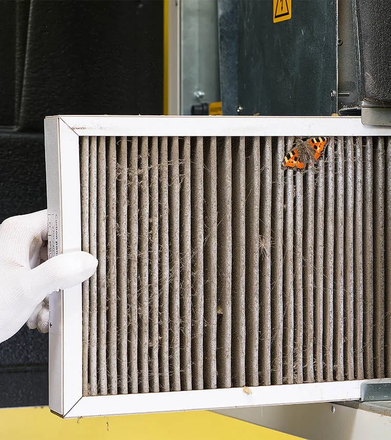 Technician removing a heavily clogged HVAC air filter from a commercial unit
