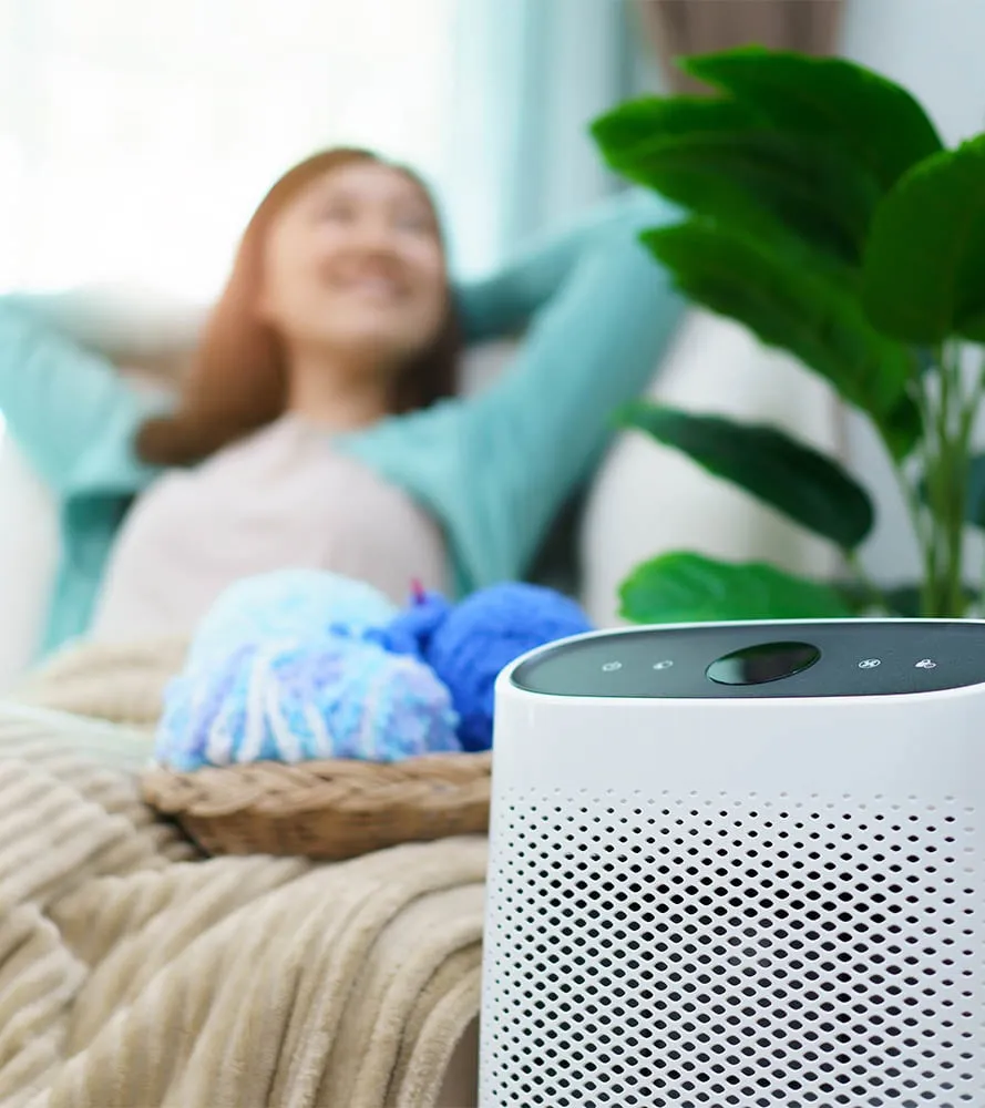 Woman relaxing comfortably at home with an air purifier in the foreground -- Cold Factor indoor air quality services