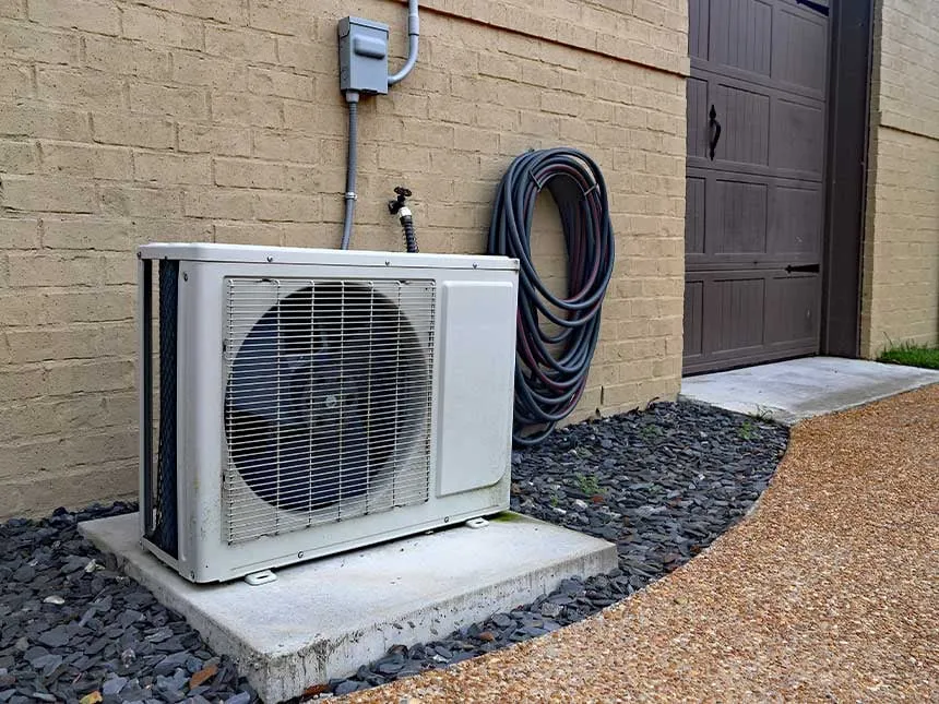 Ductless mini-split outdoor unit on a concrete pad beside a brick wall