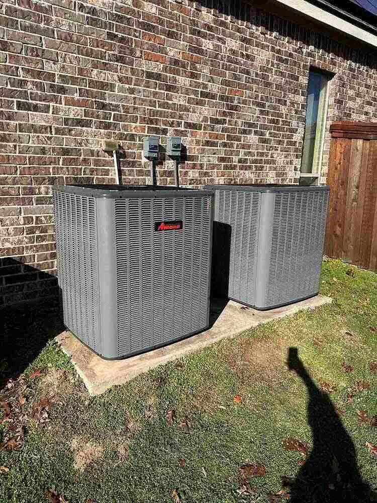 Two Amana outdoor air conditioning condenser units installed on concrete pads next to a brick home — Cold Factor HVAC installation in Flower Mound, TX