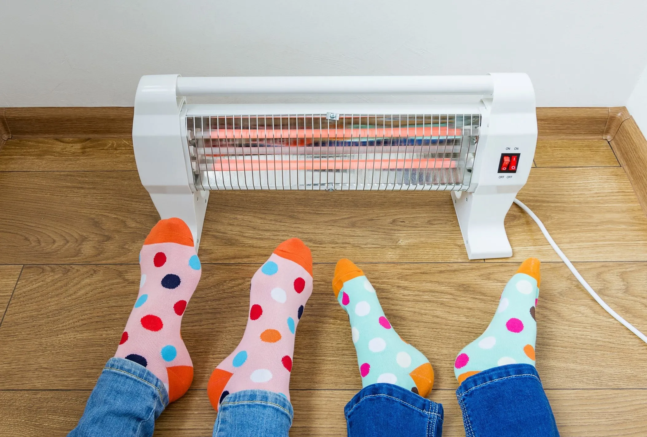 Two pairs of feet in polka-dot socks warming in front of a space heater