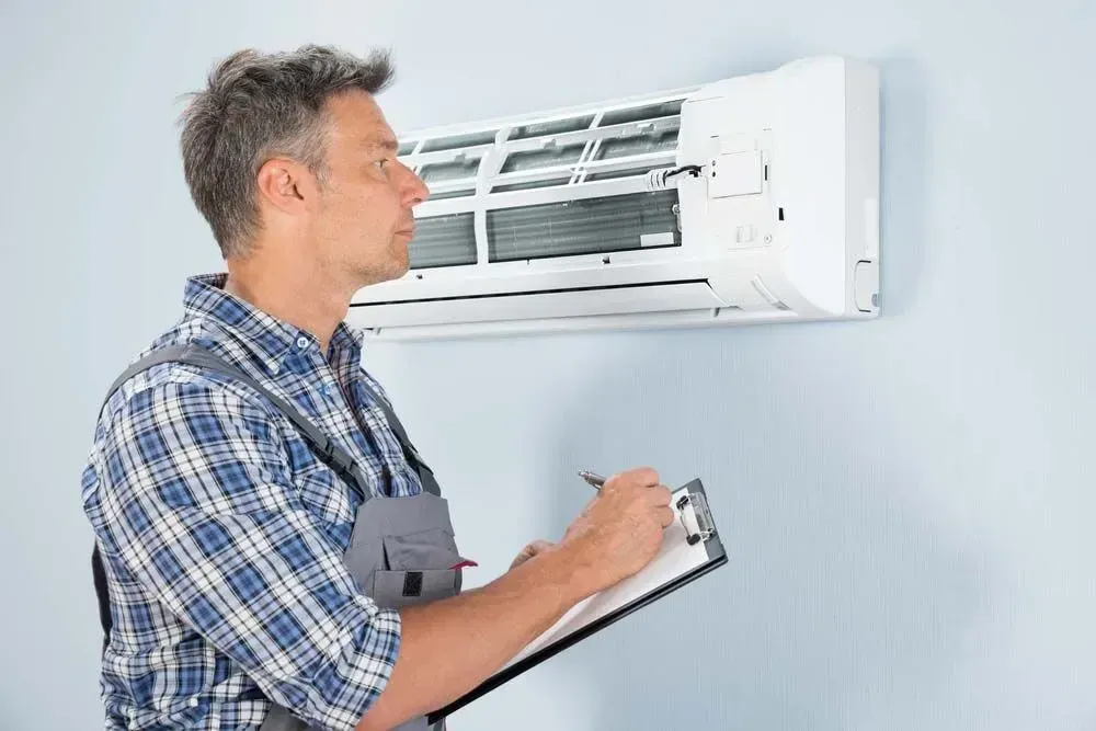 Technician with a clipboard inspecting a wall-mounted AC unit