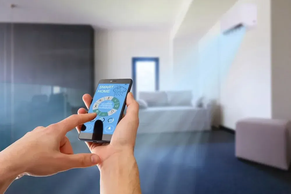 Hands using a smart home app on a phone in a room cooled by a wall-mounted AC
